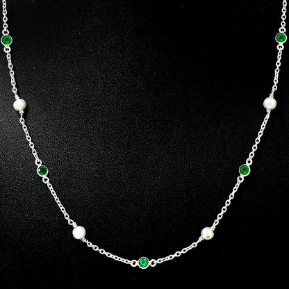 Close view of white pearls and bezel set green onyx stones on a silver chain against black
