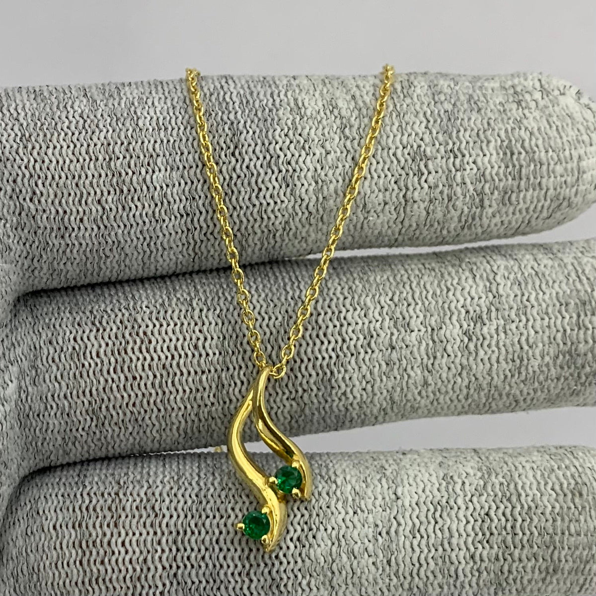 Swirl pendant with two green tourmaline stones on a gold tone chain draped over gray knit