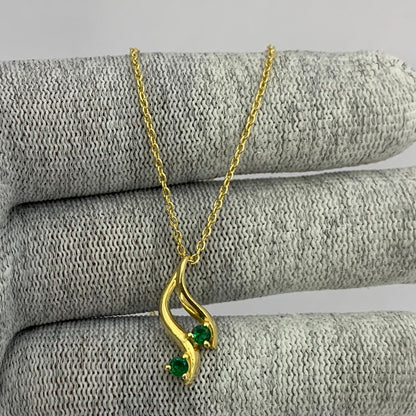 Swirl pendant with two green tourmaline stones on a gold tone chain draped over gray knit