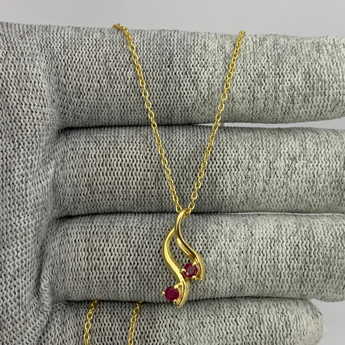 Pink rubellite swirl pendant on a gold tone chain draped over gray knit fabric