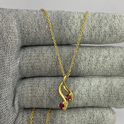 Pink rubellite swirl pendant on a gold tone chain draped over gray knit fabric