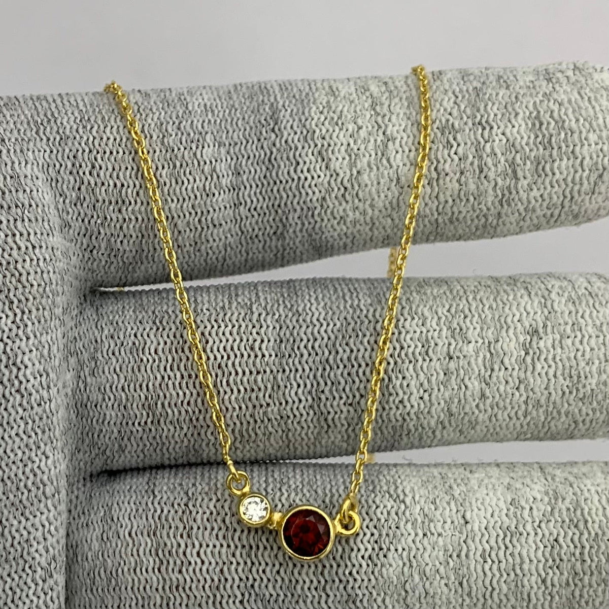 Two stone necklace with a red garnet and a small clear accent on a gold tone chain over gray knit