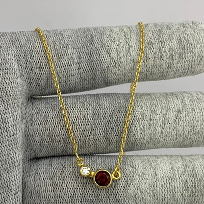 Two stone necklace with a red garnet and a small clear accent on a gold tone chain over gray knit