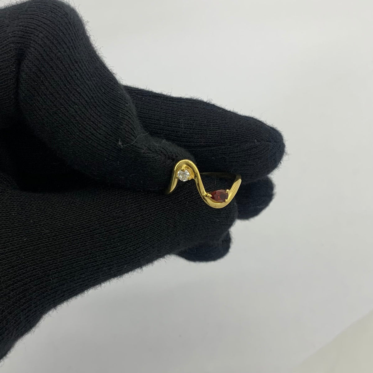 Wave ring with a pear garnet held between two gloved fingertips to show its size
