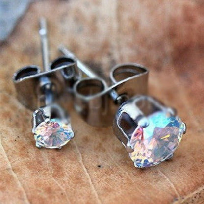Aurora borealis CZ stud earrings flashing pink and blue light, shown with steel clutches on wood