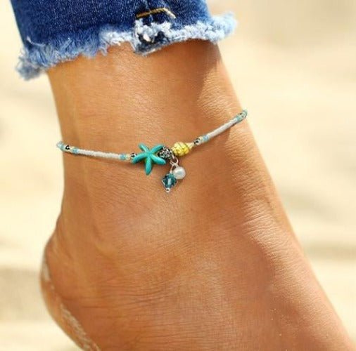 Beaded starfish anklet in white and turquoise seed beads worn above denim, the charms at the front