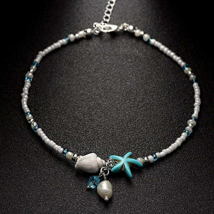 Beaded starfish anklet laid on black, showing the shell, starfish, pearl drop, blue crystal and clasp
