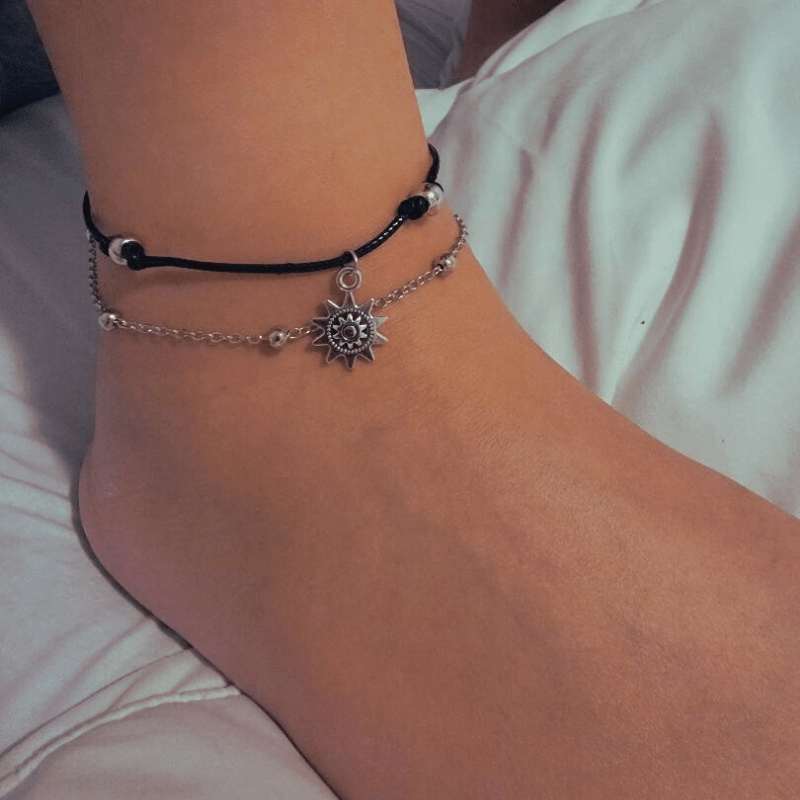 Boho sun anklet worn on the ankle, a black cord with silver beads above a chain carrying a sun charm