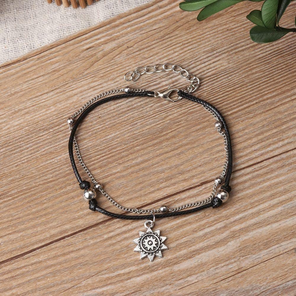 Sun anklet laid on a wooden table with its black cord, silver beads, chain, sun charm and extender