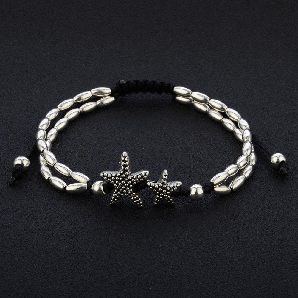Starfish anklet laid flat on black, showing two oval bead strands, twin starfish and the sliding black cord
