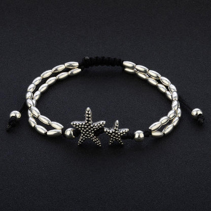 Starfish anklet laid flat on black, showing two oval bead strands, twin starfish and the sliding black cord