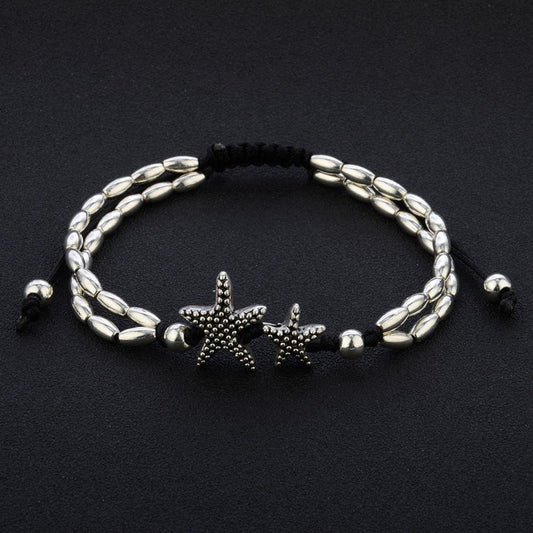 Starfish anklet laid flat on black, showing two oval bead strands, twin starfish and the sliding black cord
