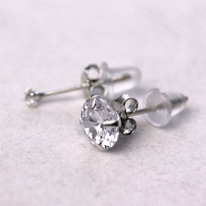 Sterling silver round CZ stud and a 2mm stud with clear rubber clutches on a white surface