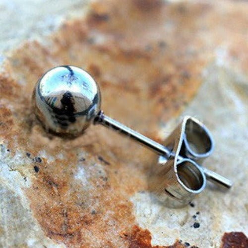 Polished surgical steel ball stud earring with its metal clutch on orange and gray stone