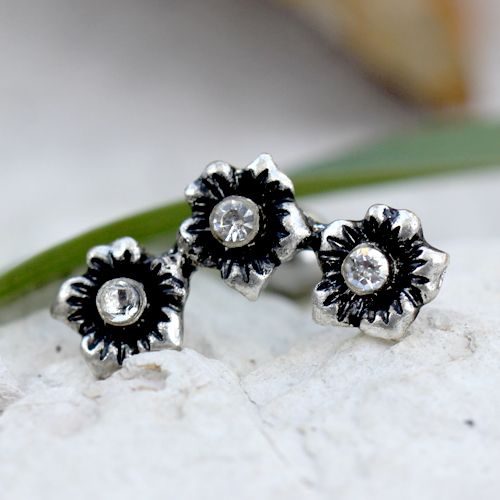 Close view of three antiqued steel flowers with clear CZ centers resting on white stone
