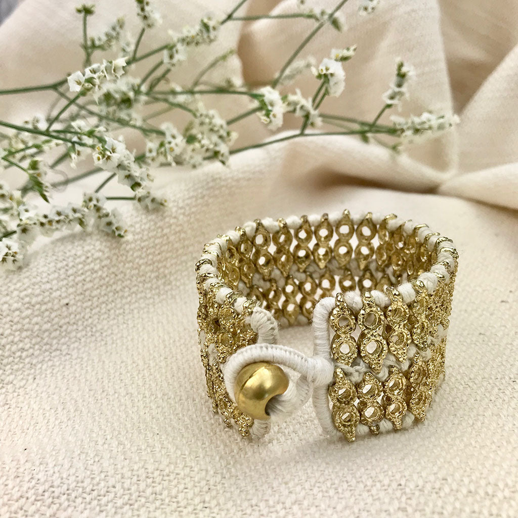 Wide woven cuff with white cotton thread and a brass tone bead closure on cream linen