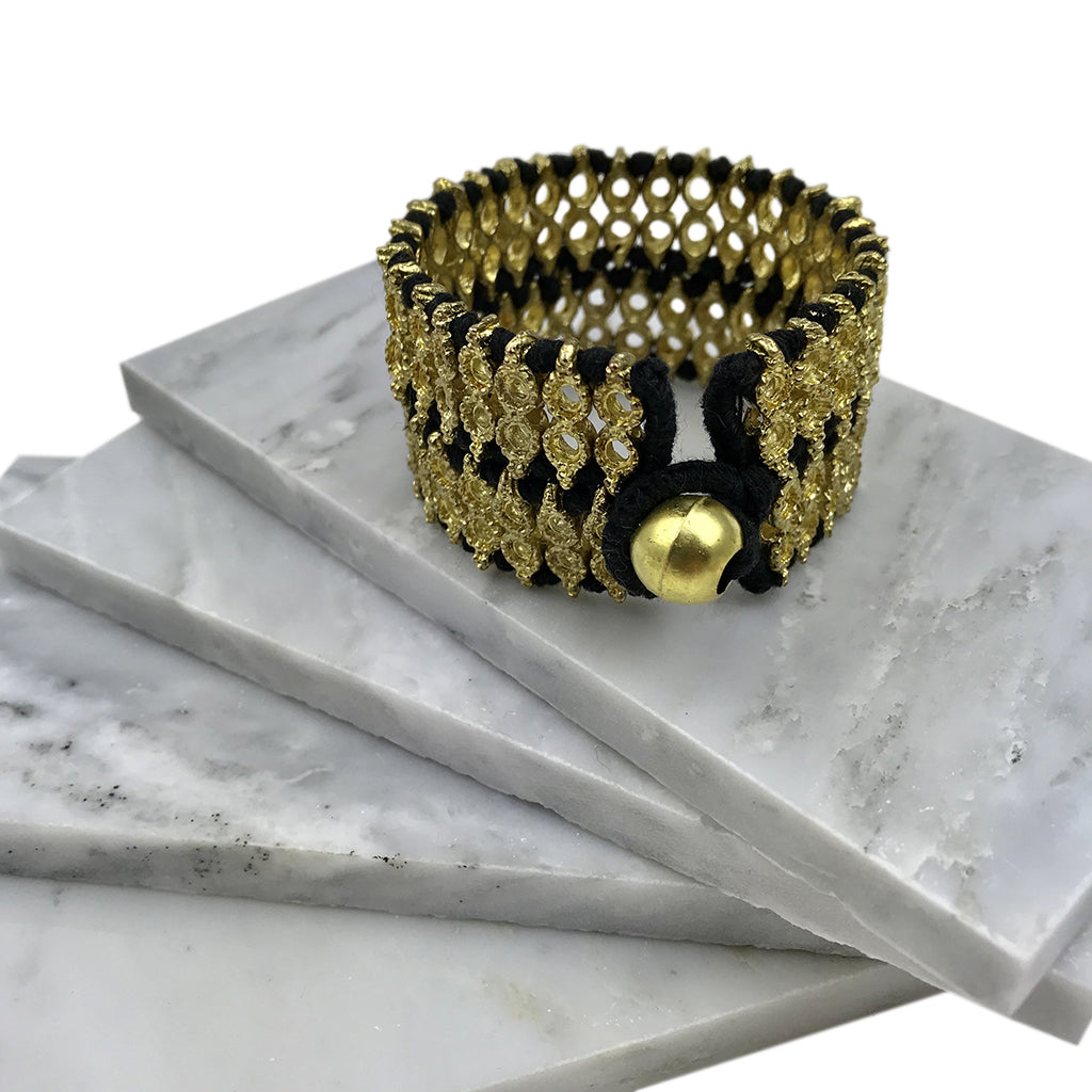 Wide woven cuff with black thread and a round bead closure resting on white marble