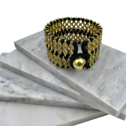 Wide woven cuff with black thread and a round bead closure resting on white marble