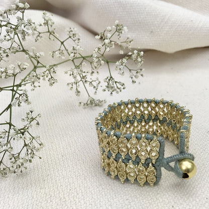 Wide woven cuff with steel blue thread and a bead closure on linen with sprigs of tiny white flowers