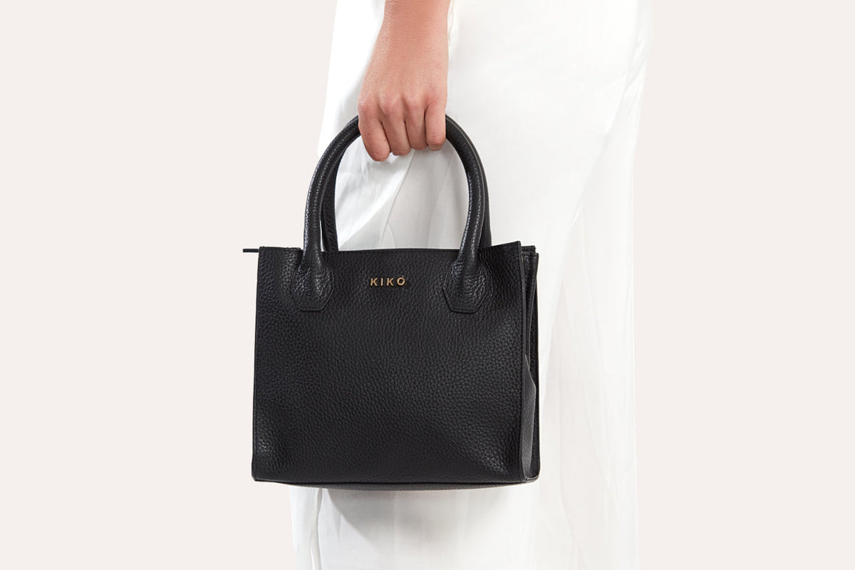 Black mini top handle bag carried by its handles against white pants