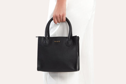 Black mini top handle bag carried by its handles against white pants