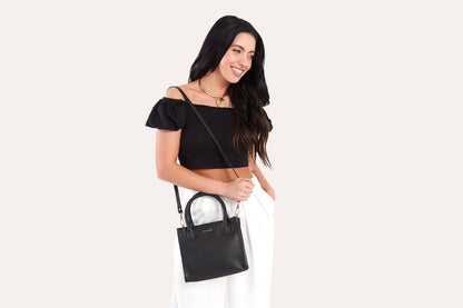 Woman in a black top wearing the black mini top handle bag across her body on its long strap