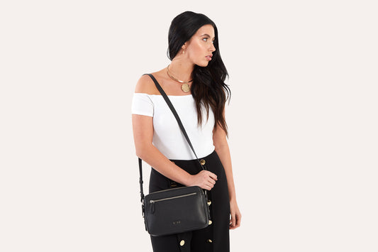 Woman in a white off-shoulder top wearing the black camera crossbody bag at her hip