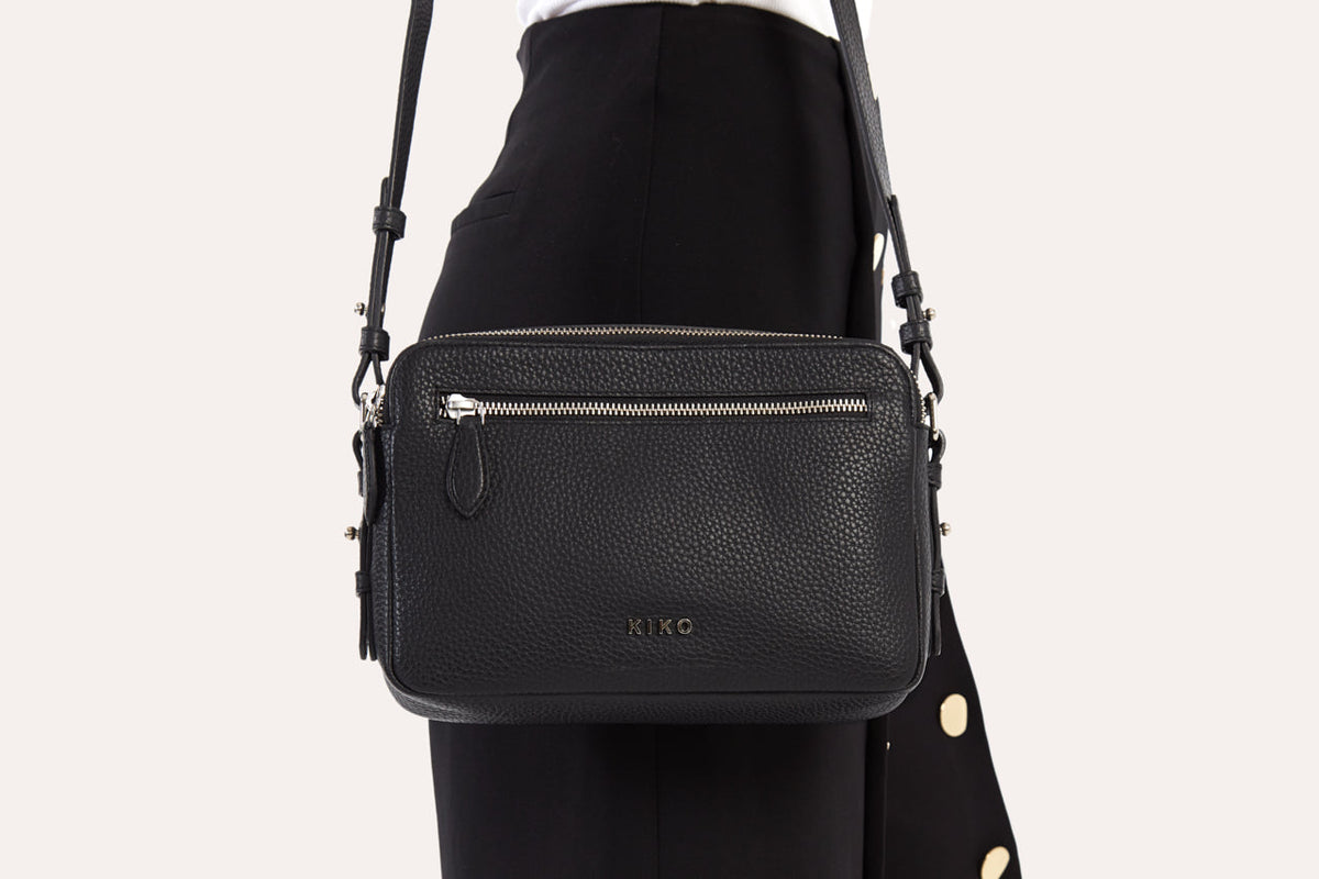 Close view of the black camera crossbody bag worn at the hip, front zip pocket and strap clips