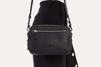 Close view of the black camera crossbody bag worn at the hip, front zip pocket and strap clips