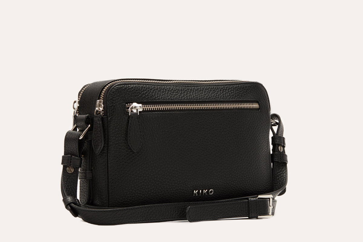 Black camera crossbody bag with its adjustable strap and buckle laid out beside it