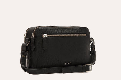 Black camera crossbody bag with its adjustable strap and buckle laid out beside it