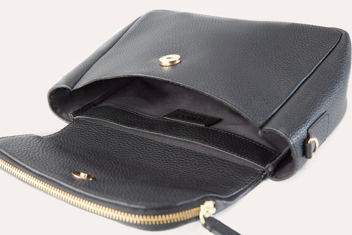Flap lifted on the black crossbody bag, showing the magnetic snap, the inside sleeve and the zip running along the flap