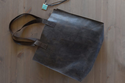 Marbled brown leather tote lying on a wood floor beside a turquoise pendant, handles fanned out