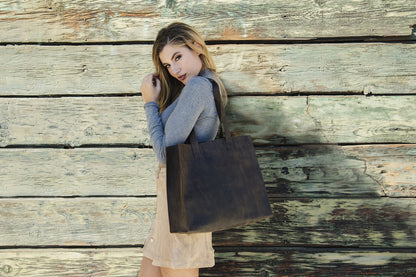 Woman leaning on a weathered wood wall with the brown leather tote on her shoulder