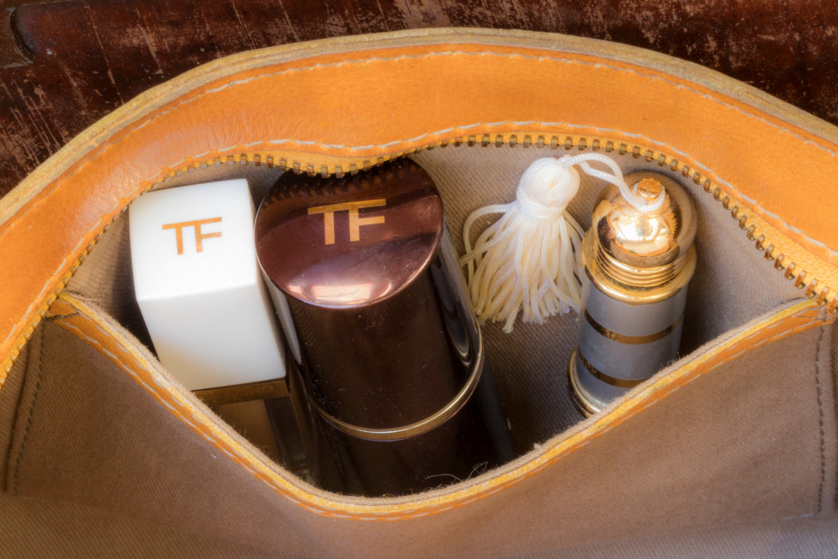 Top zip of the tan woven bag pulled open to show the fabric lining and small makeup items inside