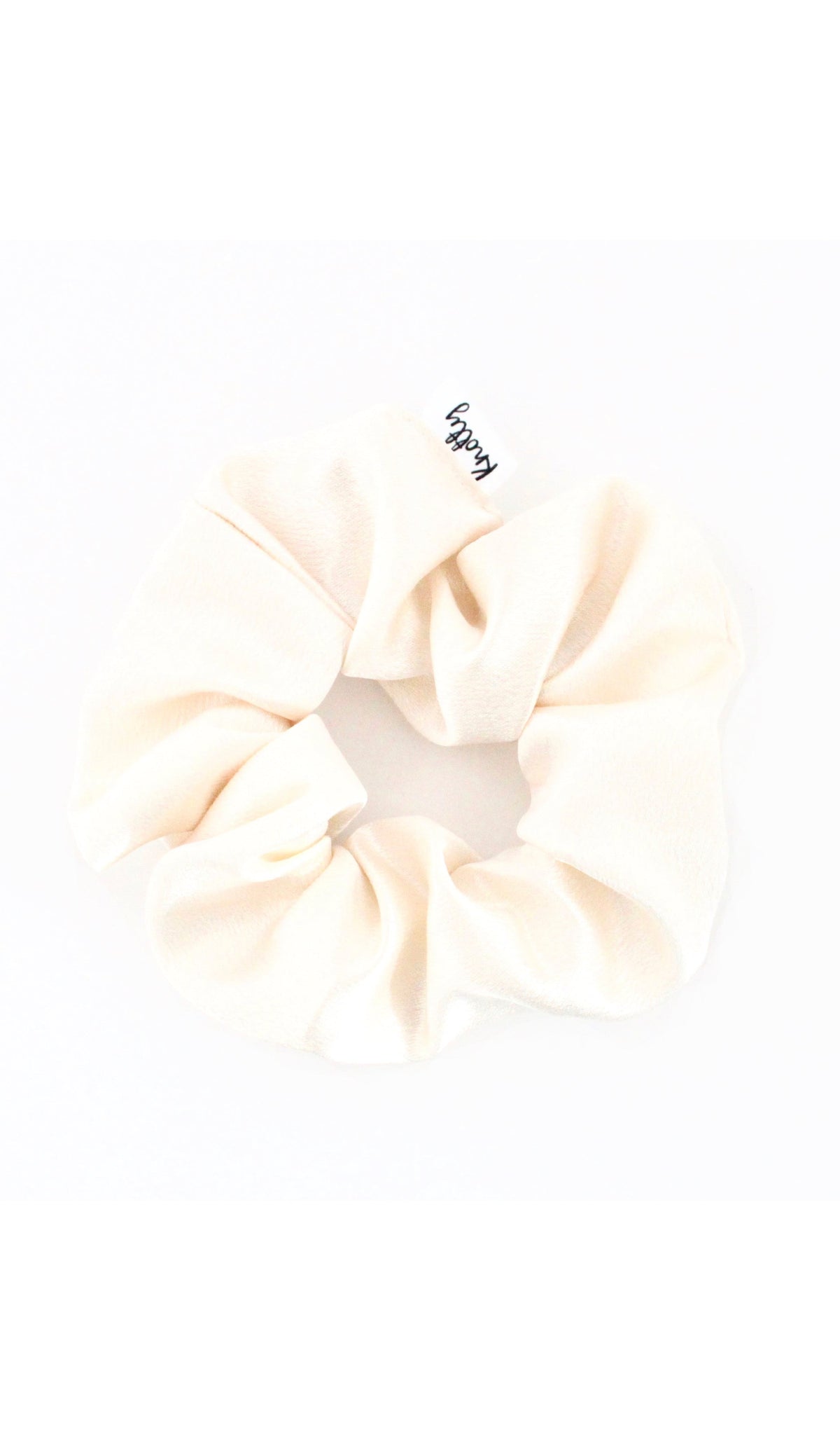 Cream washed satin scrunchie on white, gathered fabric with a small sewn label
