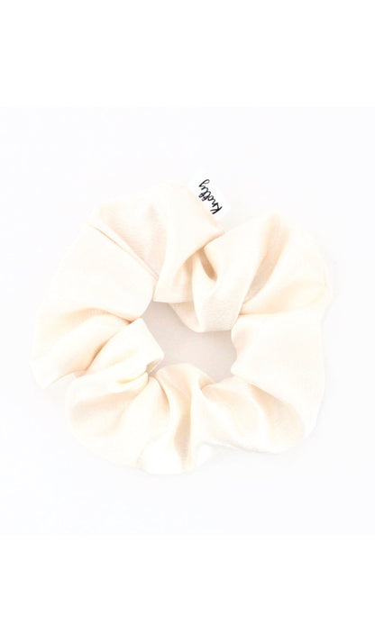 Cream washed satin scrunchie on white, gathered fabric with a small sewn label