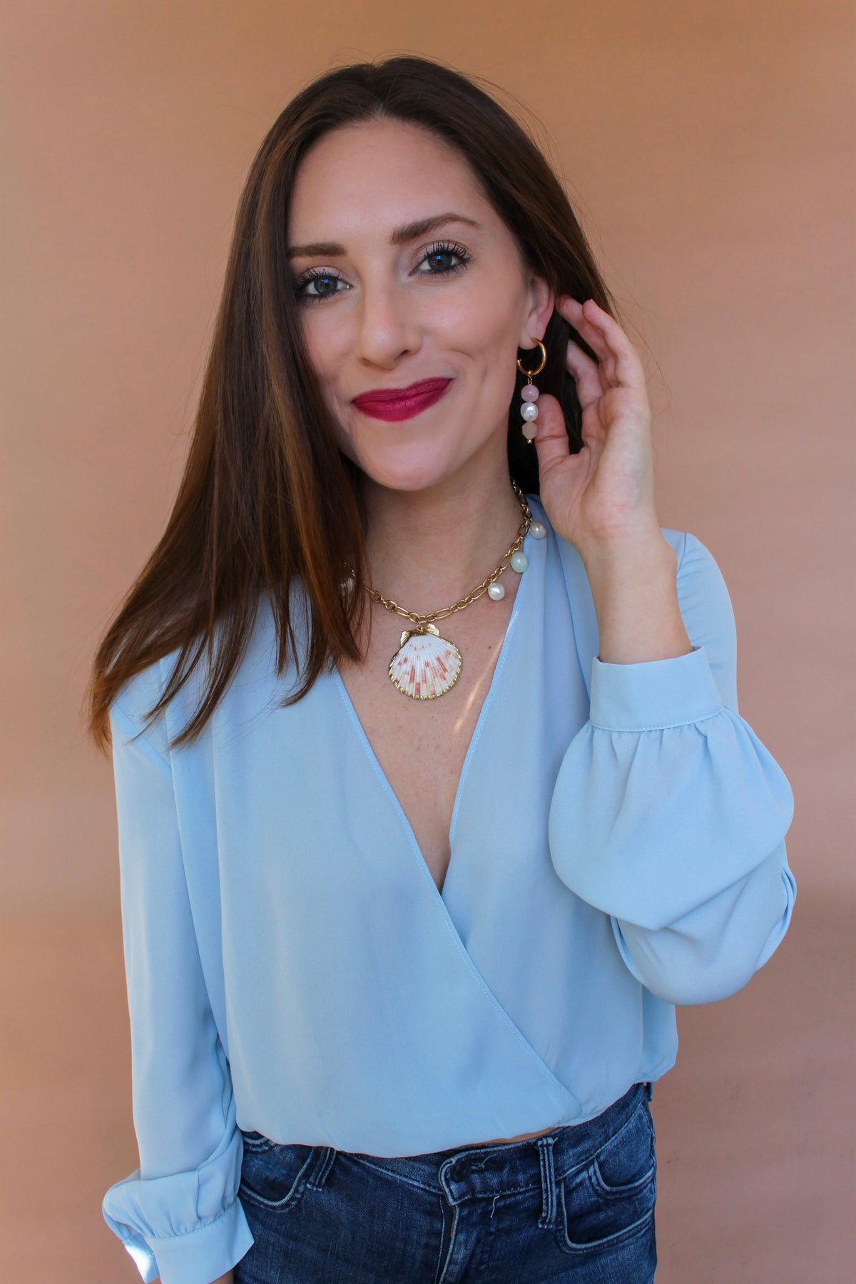 Model touching her hair to show a gemstone drop hoop earring hanging below the lobe
