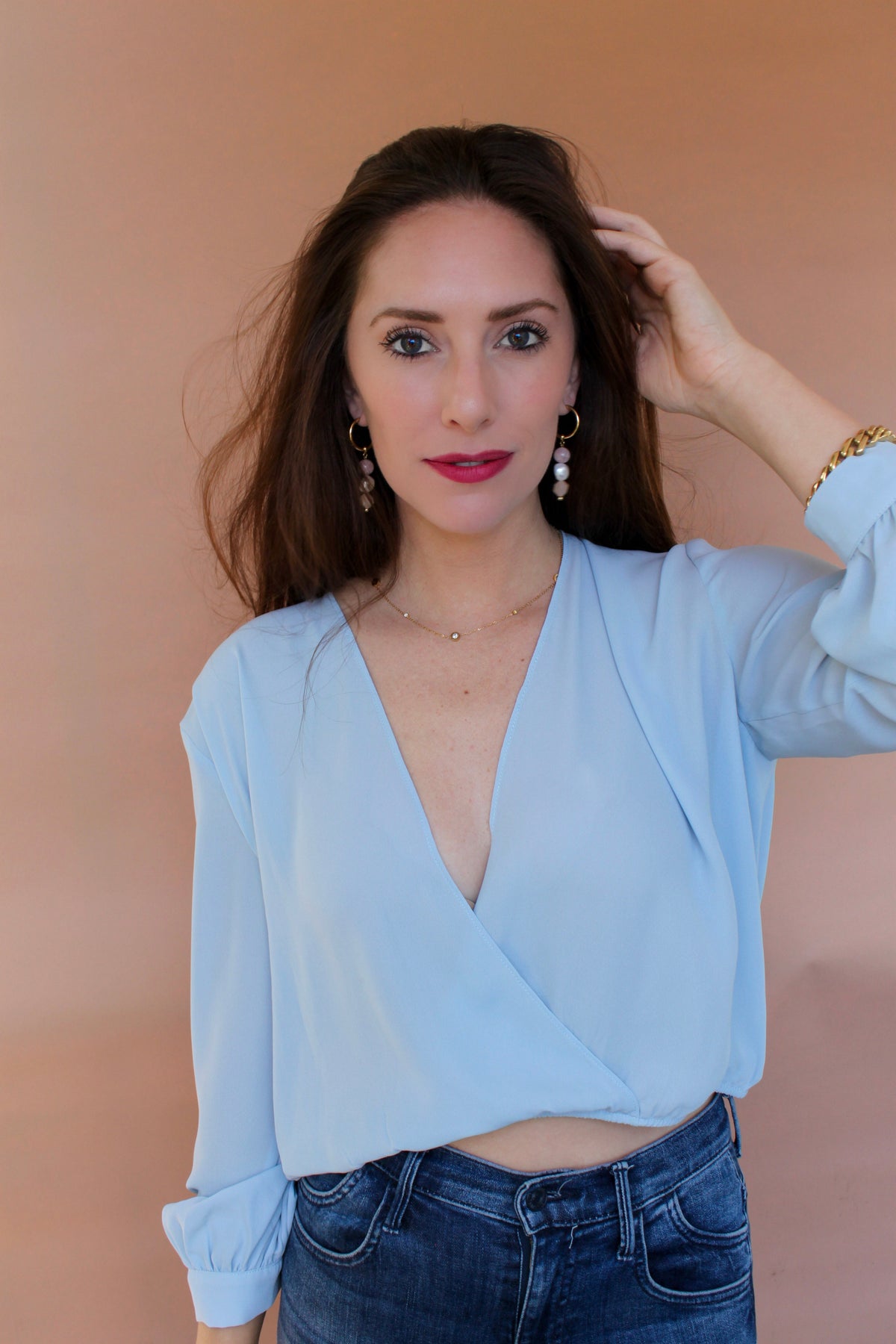 Model with one hand in her hair, gemstone drop hoop earrings on both ears, front view