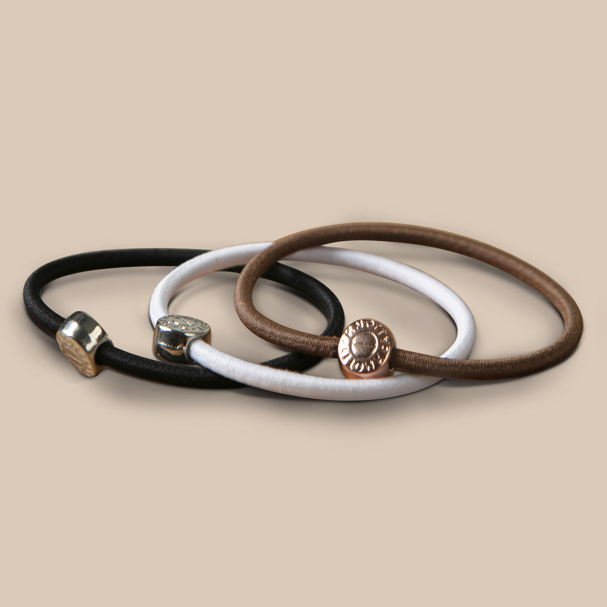 Smooth hair ties in black, white and brown, each with a round metal bead, on a beige surface