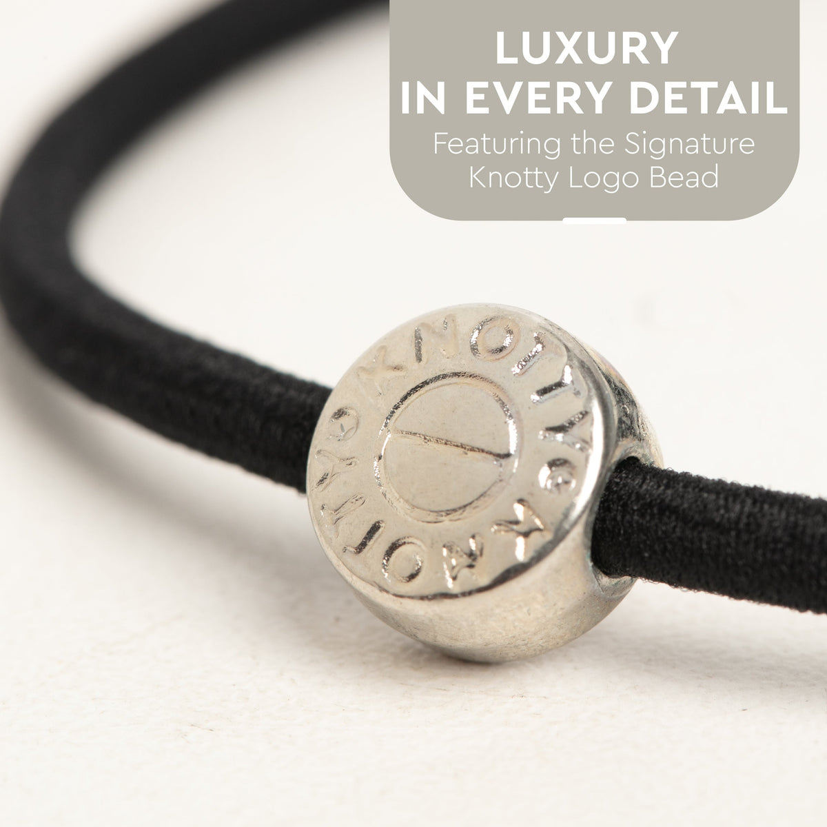 Close up of a black hair tie with a round silver tone bead engraved with a logo