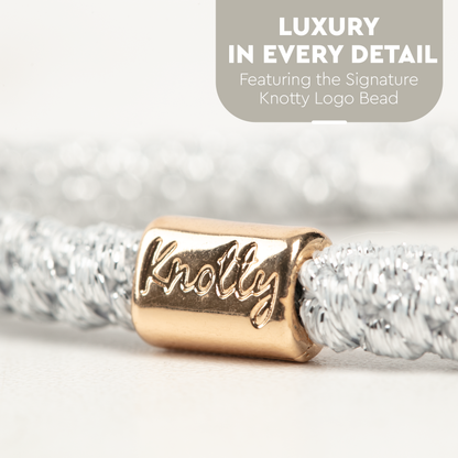 Close up of a silver metallic hair tie with an engraved gold tone bead