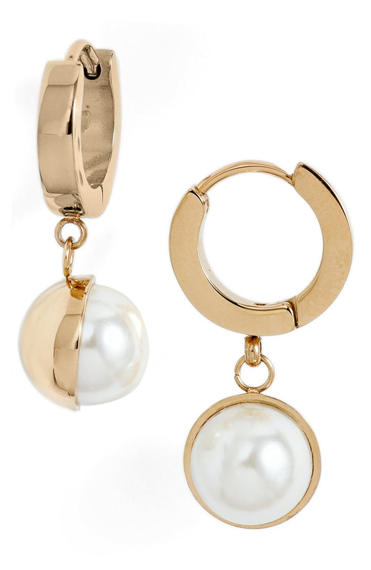 Pearl drop huggie earrings in gold tone stainless steel, one turned to show the faux pearl in its half cup