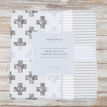 Packaged gray cross and pencil stripe bamboo muslin throw blanket on a whitewashed wood background