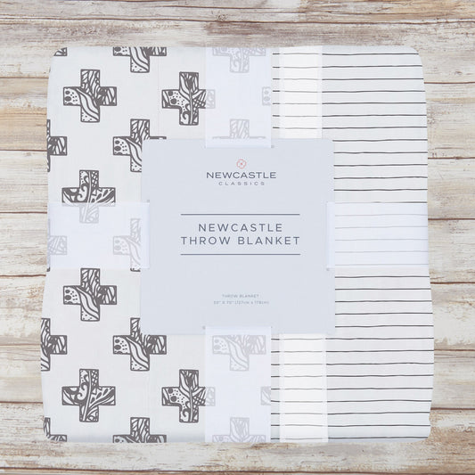 Packaged gray cross and pencil stripe bamboo muslin throw blanket on a whitewashed wood background
