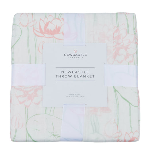 Folded bamboo muslin throw blanket in its band, printed with pink water lilies, lily pads and green stems