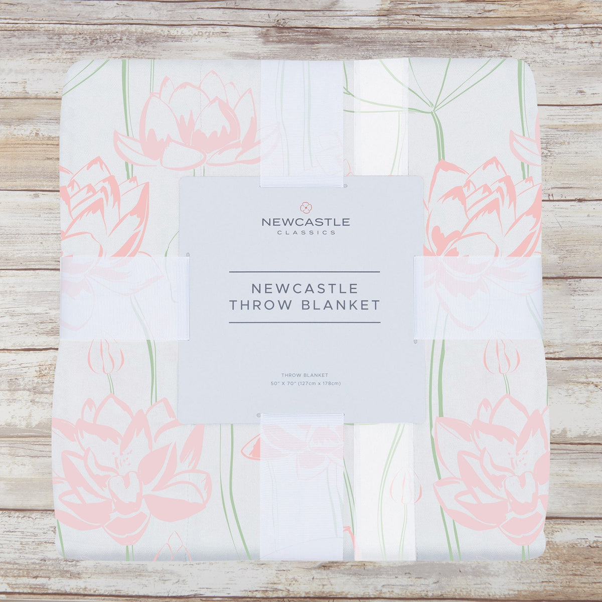 Packaged pink water lily bamboo muslin throw blanket on a whitewashed wood background