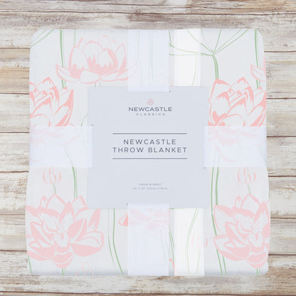 Packaged pink water lily bamboo muslin throw blanket on a whitewashed wood background