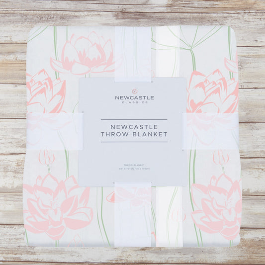 Packaged pink water lily bamboo muslin throw blanket on a whitewashed wood background