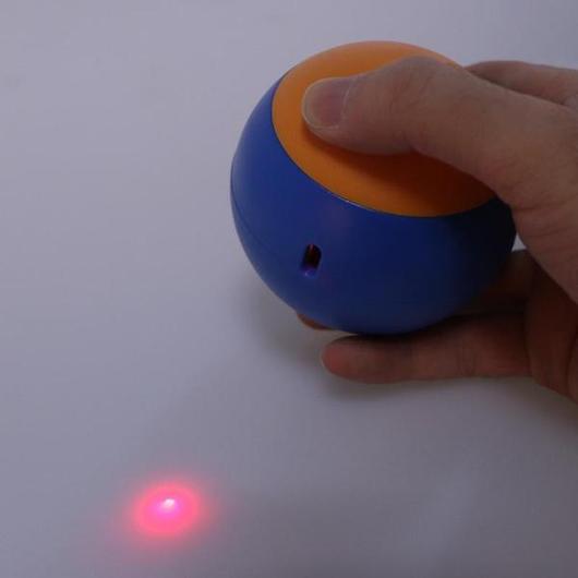 Hand pressing the orange top button on the blue ball base while a red laser dot shines on the floor